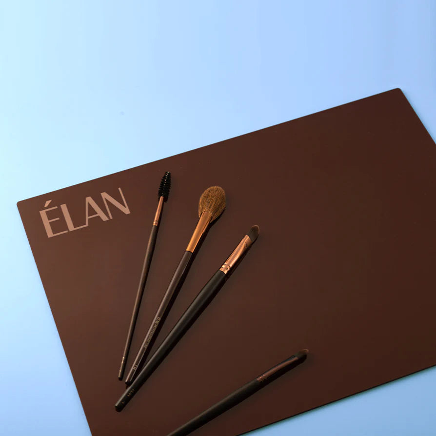 Élan Table Protector Palette in dark brown, featuring the Élan logo in the corner and arranged with four professional brushes including a spoolie, powder, and angled brush, displayed on a blue background