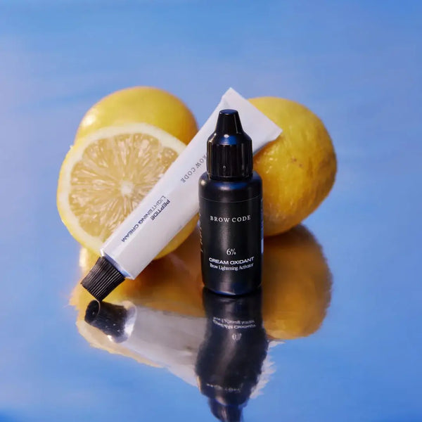 Brow Code Professional Brow Lightening System with 6% cream oxidant and lightening cream, displayed on a reflective surface with lemons