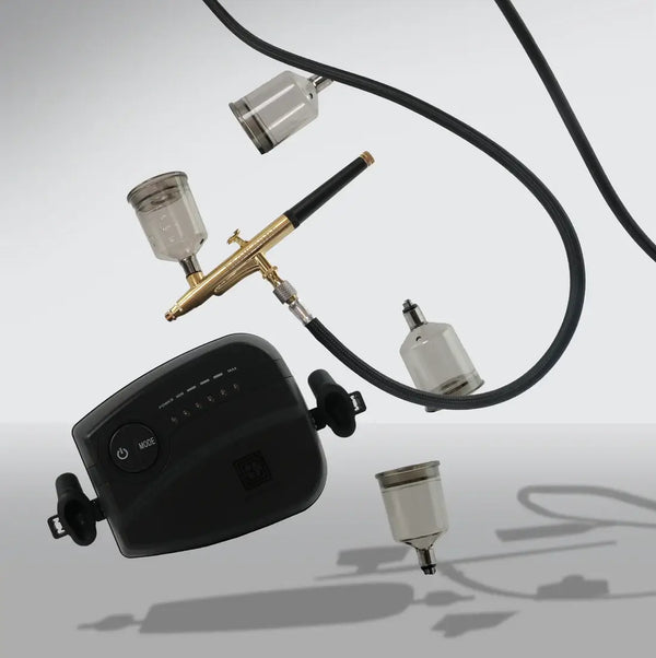 Floating Brow Code Airbrush Machine components, including a black compressor, gold airbrush pen, black hose, and detachable cups, highlighting its sleek, professional design