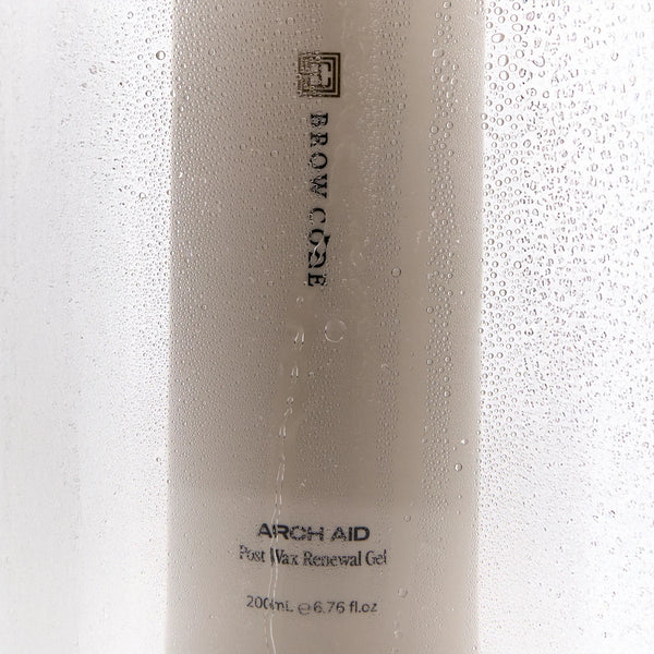 Brow Code Arch Aid Post Wax Renewal Gel behind a steamy glass surface with water droplets, emphasizing hydration and skin relief