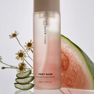 Brow Code First Base Ceramide Foaming Cleanser surrounded by natural ingredients, including aloe vera slices, chamomile flowers, and a fresh watermelon wedge