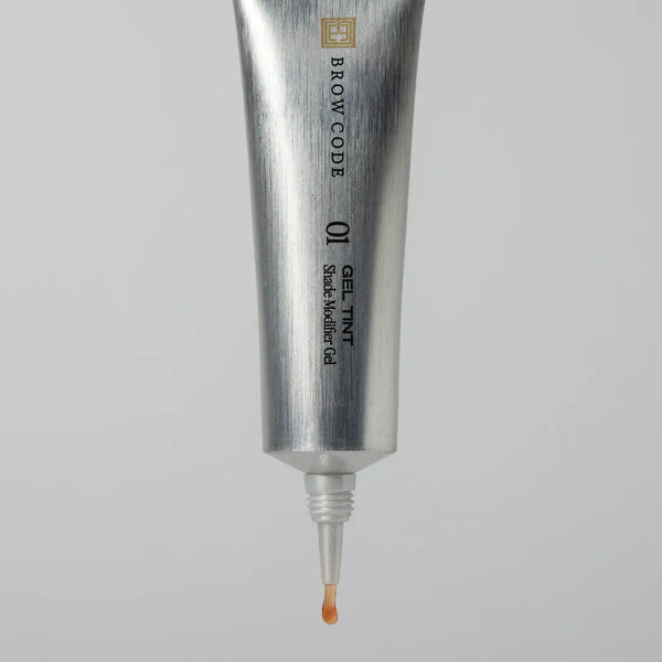 Silver tube of Brow Code gel tint with applicator on a gray background