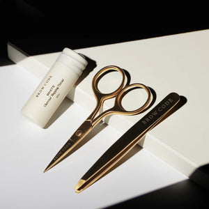 Brow Code Mapping Kit tools in shadowed light, featuring white charcoal thread, gold trimming scissors, and precision tweezers on display
