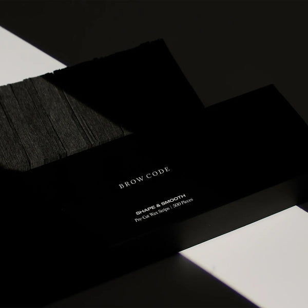 Brow Code Shape & Smooth Pre-Cut Wax Strips box in matte black, holding 500 strips for precise professional eyebrow waxing