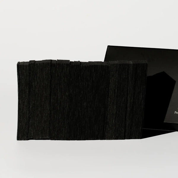 Brow Code Pre-Cut Wax Strips in black, neatly stacked and fanned out, partially emerging from a sleek black box with minimal branding, designed for precise eyebrow shaping