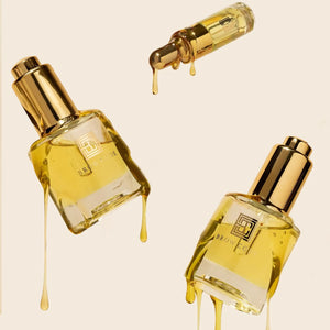 Brow Code Brow Gold Oil dripping from luxurious glass bottles with golden caps, designed for nourishing and strengthening eyebrows