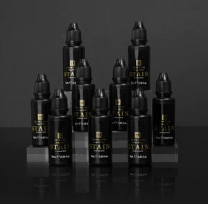 Brow Code Stain Hybrid Dye full collection displayed in a tiered arrangement, featuring 10 professional-grade 15ml bottles for brow tinting in multiple shades