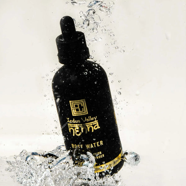 Black bottle of Brow Code Henna Rose Water with water droplets on a light gray background