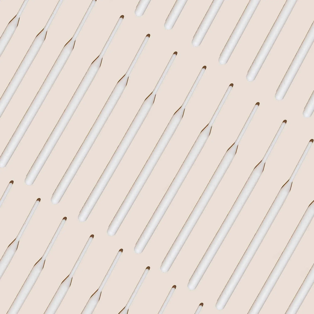 Brow Code Tinting Sticks 25-pack displayed in a diagonal pattern on a beige background, featuring sleek white sticks for precise brow application