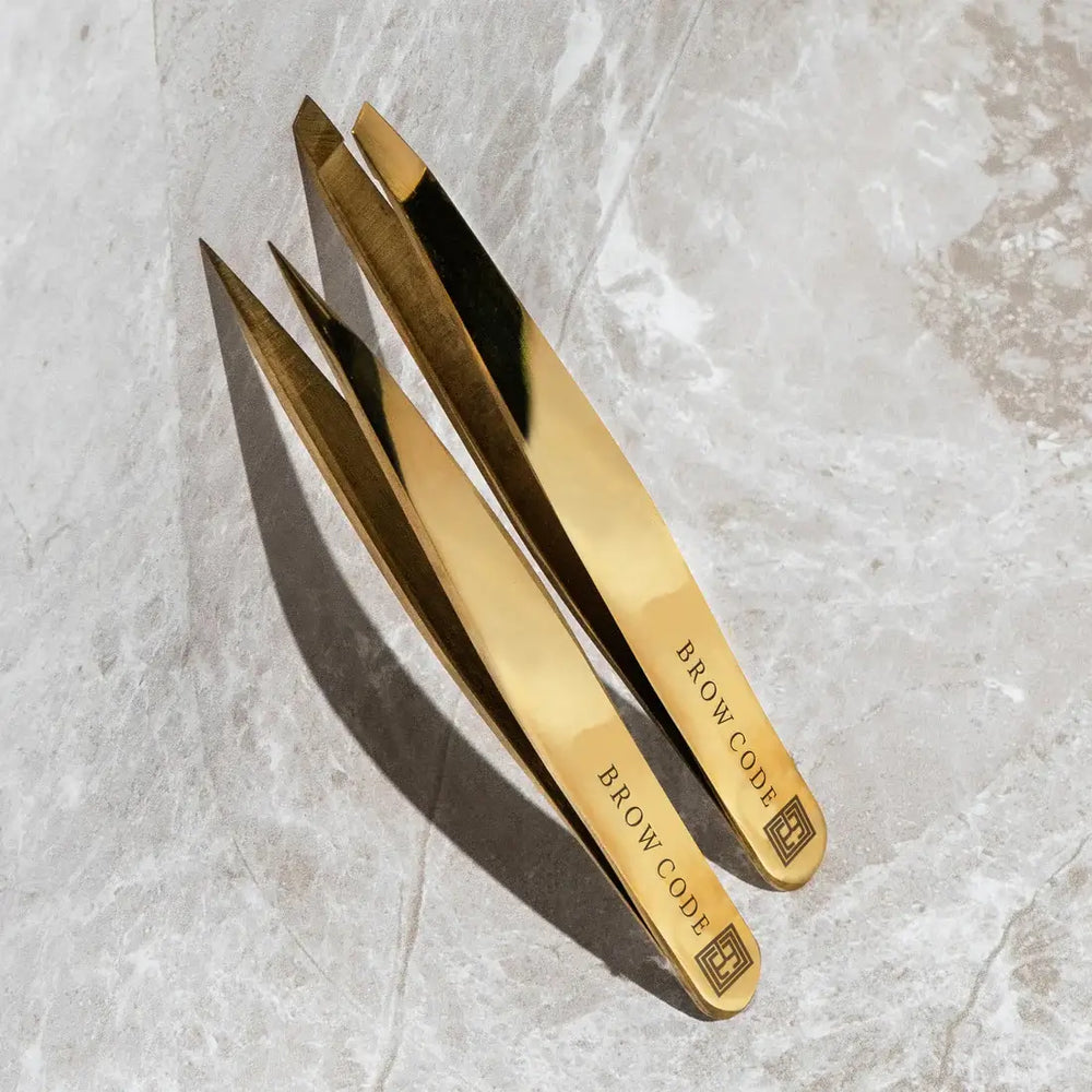 Brow Code gold stainless steel tweezers set featuring precision tip and slant tip designs, ideal for professional eyebrow shaping and grooming