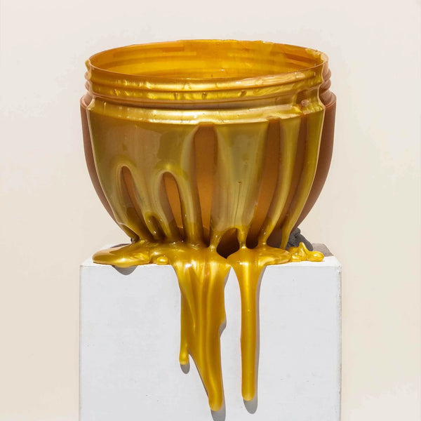 Overflowing golden jar of melted Brow Code Microwavable Brow Wax dripping down a white platform, showcasing its smooth, golden consistency