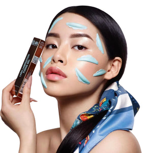 Model with smooth skin and cloud-shaped patches on face holding ÉLAN Lash Lamination Fixing Gel box, promoting a lash lamination product in a stylized beauty shoot.